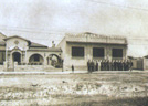Fotografia antiga em tons sépia de uma fachada com construções e muro